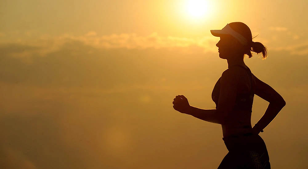 Outline of Woman Jogging with Bright Sun in Background